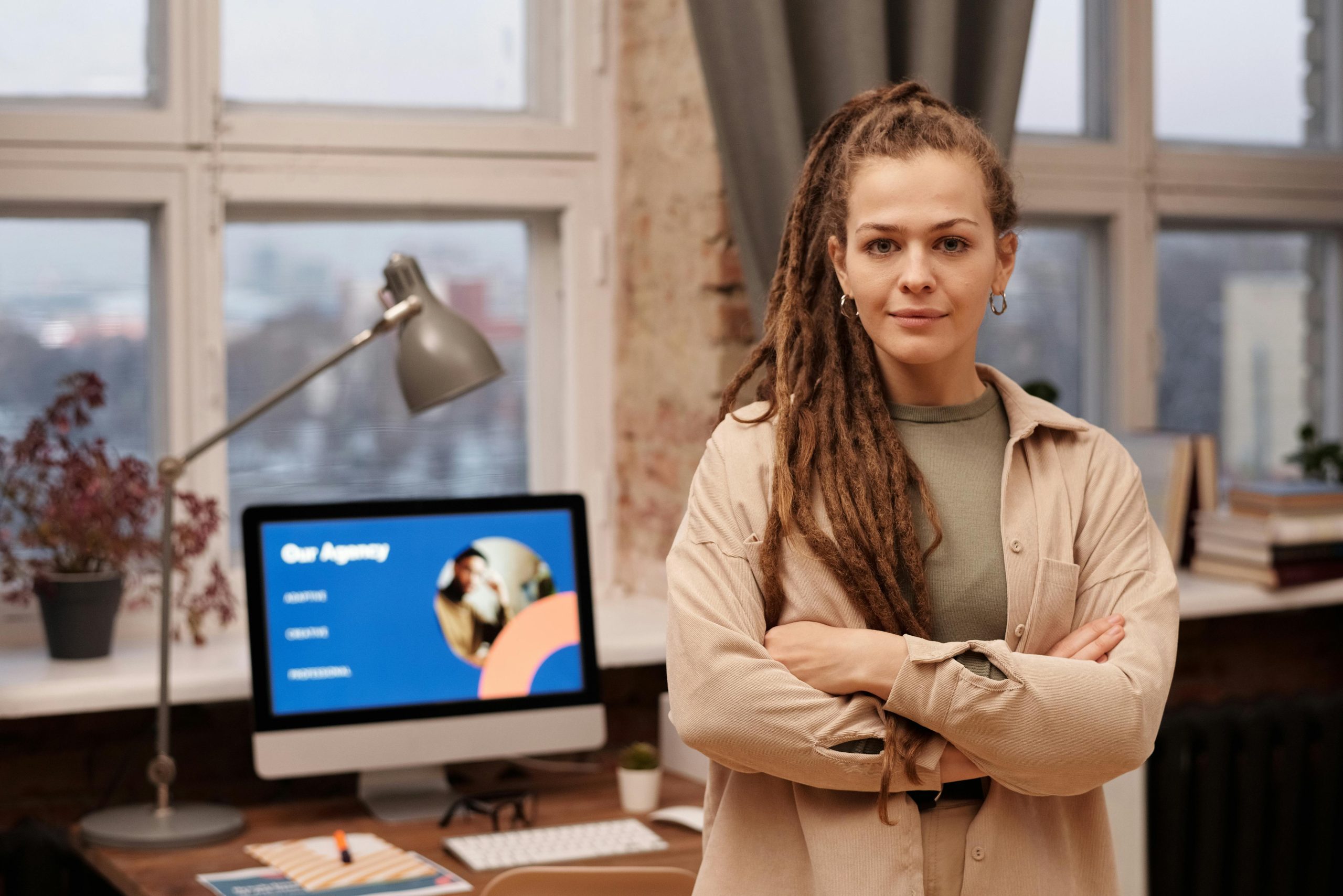 A young woman with dreadlocks stands confidently in a home office setting.