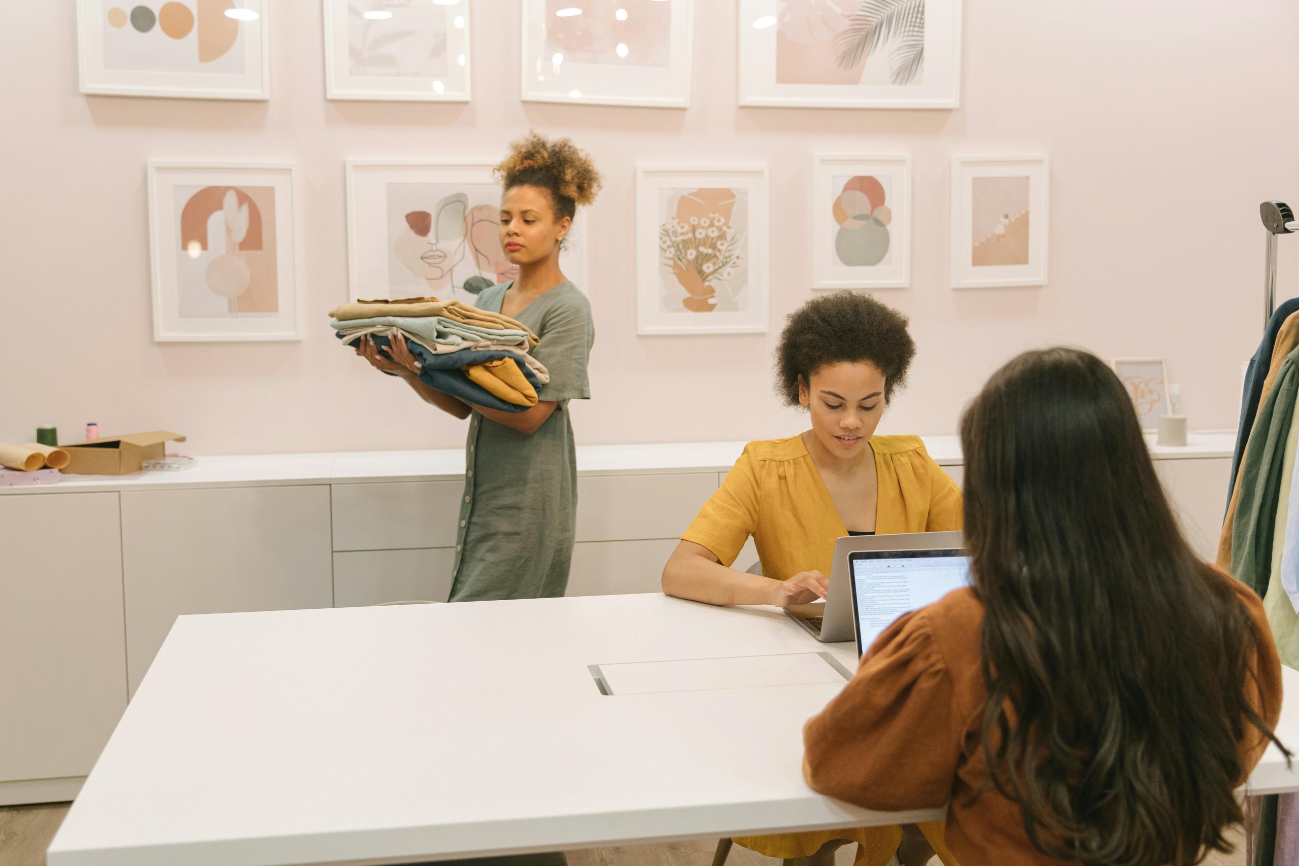 Three women working together in a stylish office setting, focusing on teamwork and clothing business.